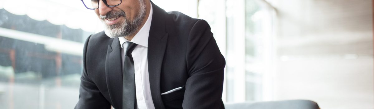 Smiling senior businessman checking message on phone and smiling when receiving good news. Cheerful man surfing net in hotel hall. Business travel concept